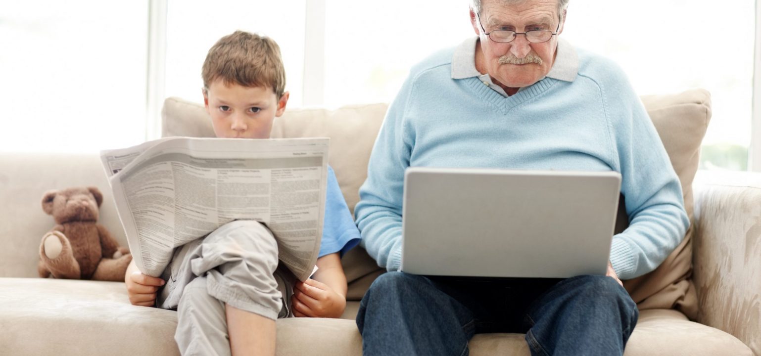 Old man using a laptop with his grand son reading a newspaper - Indoor