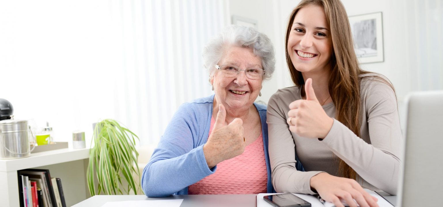 young woman helping an old senior woman doing paperwork and administrative procedures with laptop computer at home